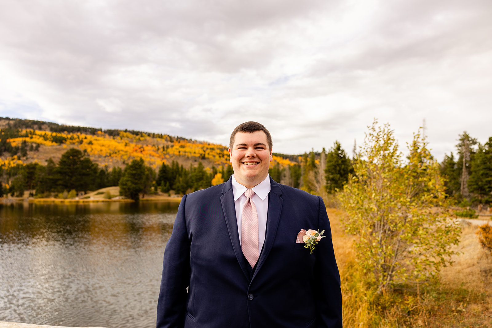 happy groom in a blue suit smiling before his Fall elopement at Sprague Lake. 
